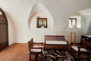Une pièce avec un mur blanc à la texture particulière, deux fenêtres à cadre en bois, un tapis à motifs et des meubles en bois.
