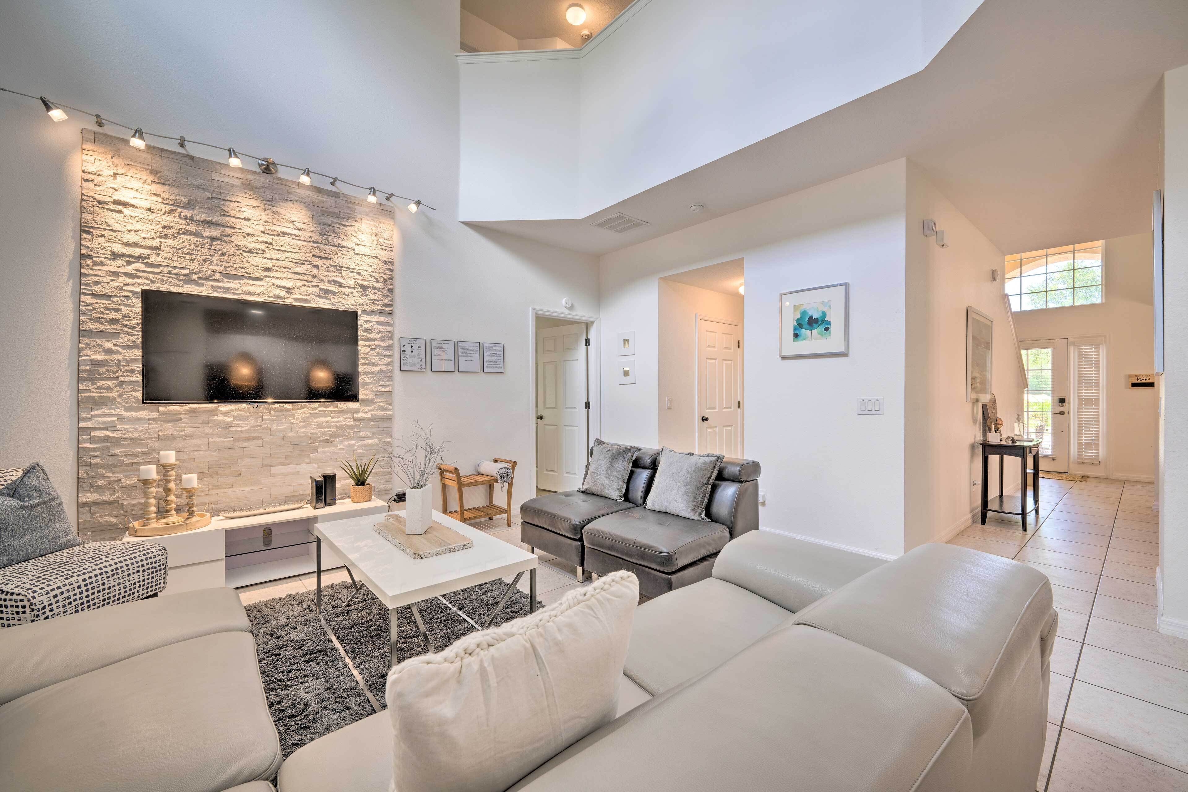 A spacious living room with a stone accent wall, a flat-screen TV, and a grey leather sofa.
