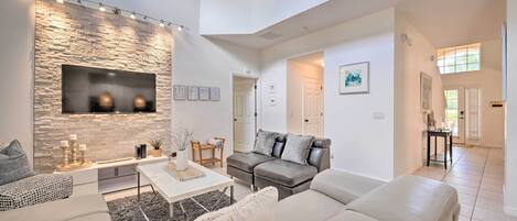 A spacious living room with a stone accent wall, a flat-screen TV, and a grey leather sofa.