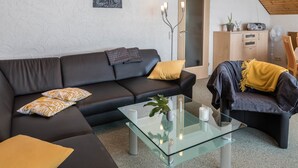 Un salon moderne avec un canapé en cuir noir, une table basse en verre et un meuble en bois.