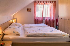 A bedroom with two beds, a nightstand, a lamp, a radiator, and a window with curtains.