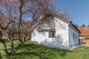 A white building with a small window and a door, surrounded by a well-maintained lawn and flowering trees.
