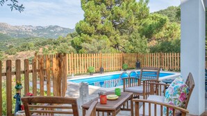 A wooden deck with a pool, outdoor furniture, and a view of trees and mountains.