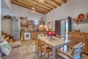 A kitchen with wooden beams, a dining table with chairs, a washing machine, and a refrigerator.