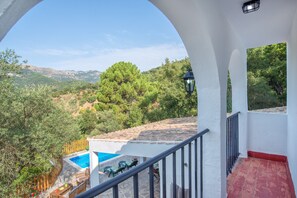 A balcony with a pool, outdoor furniture, and a view of a mountainous landscape.
