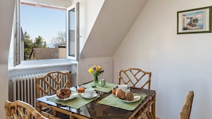 Un rincón comedor con una mesa dispuesta para dos, sillas de mimbre, vista a través de un ventanal y un cuadro en la pared.