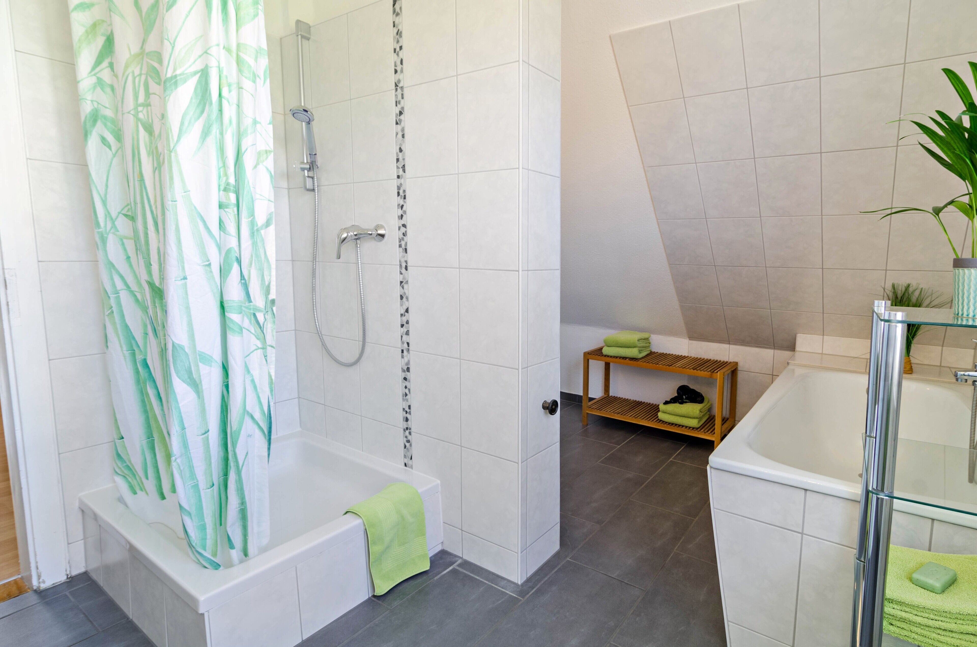 Un bany modern amb dutxa, banyera, un lavabo amb vidre i una petita estant amb tovalloles.