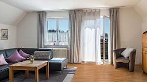 Una sala de estar moderna con sofá, una mesa de centro, una silla y vistas al exterior a través de un amplio ventanal.