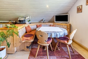 Una habitación acogedora con un banco de madera, una mesa con mantel blanco y un televisor en la pared.