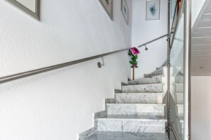 A marble staircase with a metal handrail, white walls, and a framed picture on the upper landing.