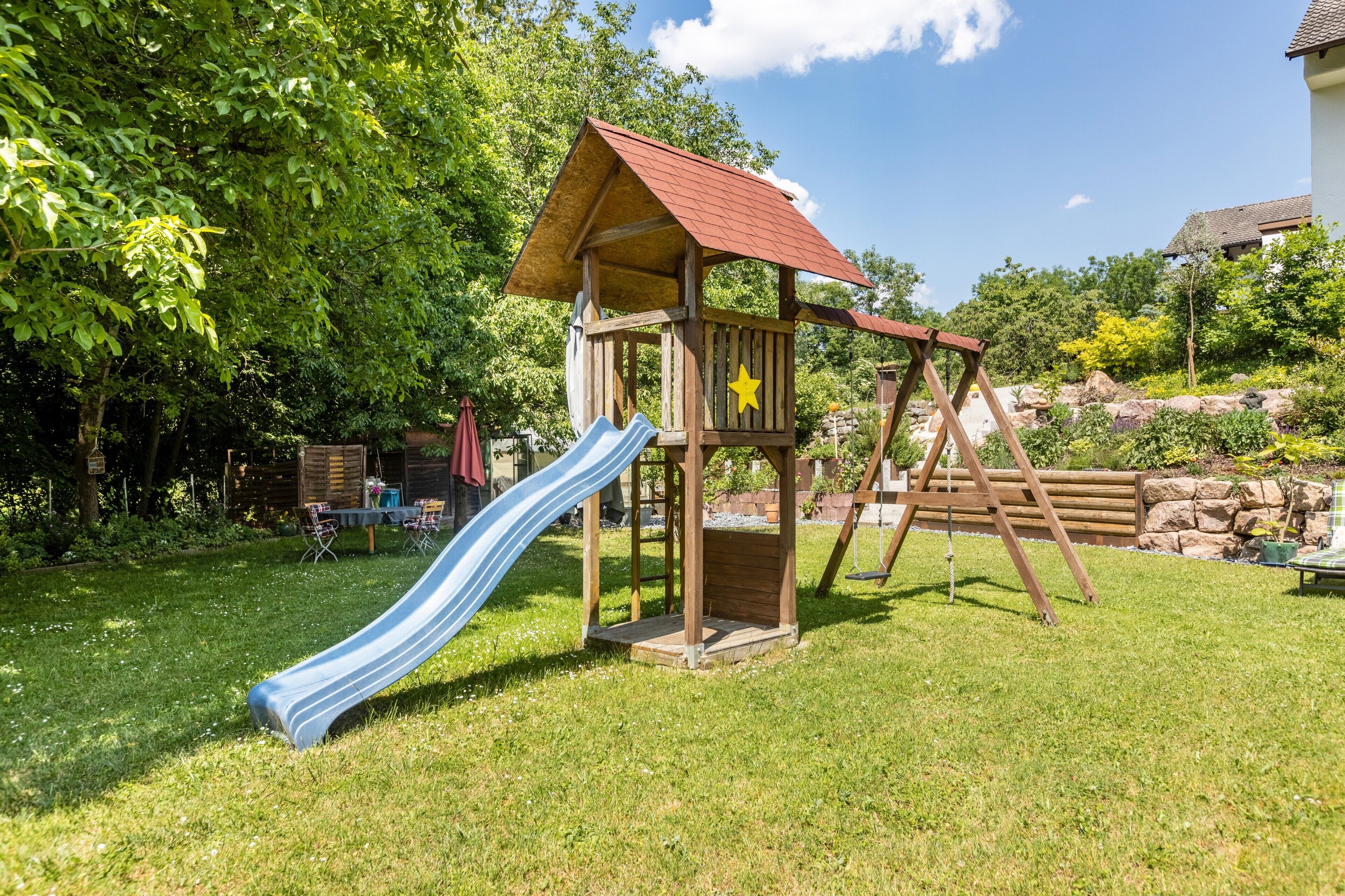 A wooden play structure with a slide and a swing set in a grassy backyard.