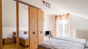 Un dormitorio con cama, armario de madera, escritorio con silla y ventana con cortinas.