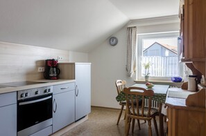 A compact kitchen with a stove, oven, and coffee maker, a dining table with chairs, and a window with curtains. - Apartment "Roth" near Lake Constance with Lake View and Wi-Fi (Überlingen)