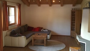 Ein gemütliches Wohnzimmer mit Holzbalkendecke, einer Sofagarnitur, einem Couchtisch und einem Kamin.