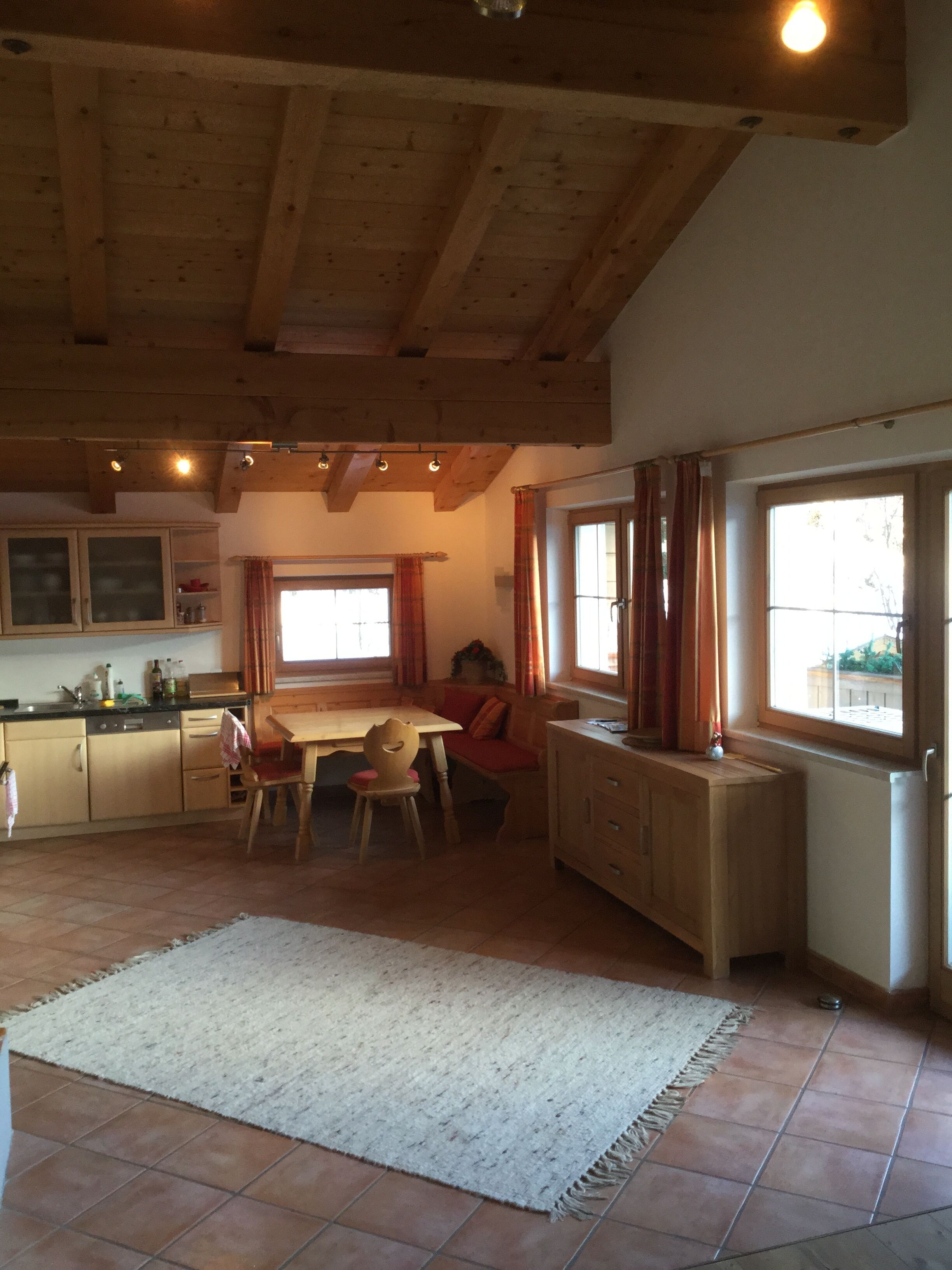 A spacious kitchen with wooden beams, a dining area with a table and chairs, and a large window with curtains.