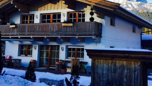 Eine zweistöckige Chalet mit Balkon, Holzfassade und Blick auf schneebedeckte Berge.