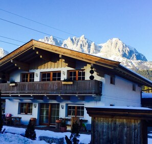 A two-story chalet with a balcony, wooden exterior, and a view of snow-covered mountains. - Ferienwohnung Going Home (Going am Wilden Kaiser)