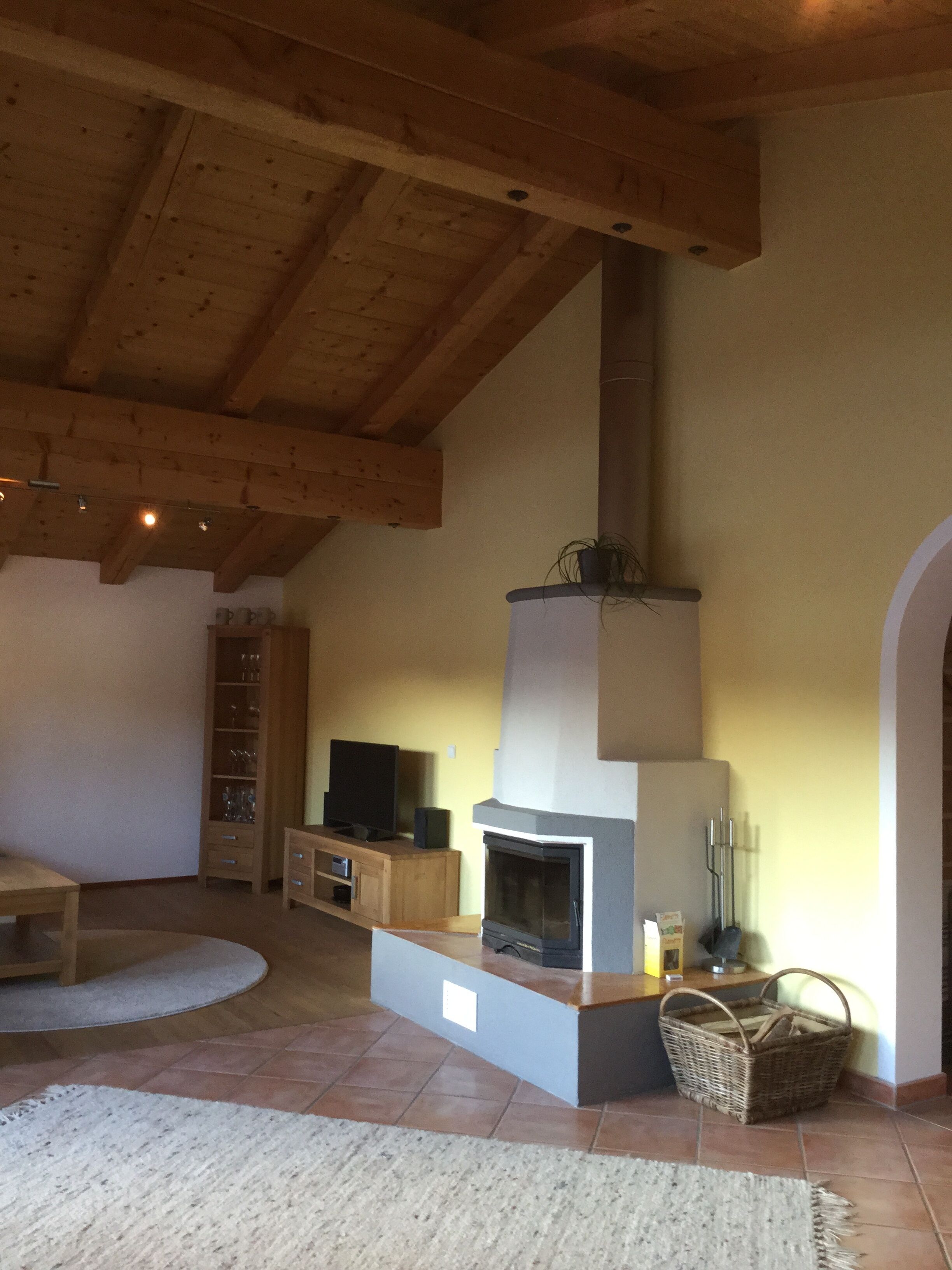Uma sala de estar com lareira, vigas de madeira, televisão e estante de livros.