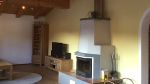 Ein Wohnzimmer mit Kamin, Holzbalken, Fernseher und Bücherregal.