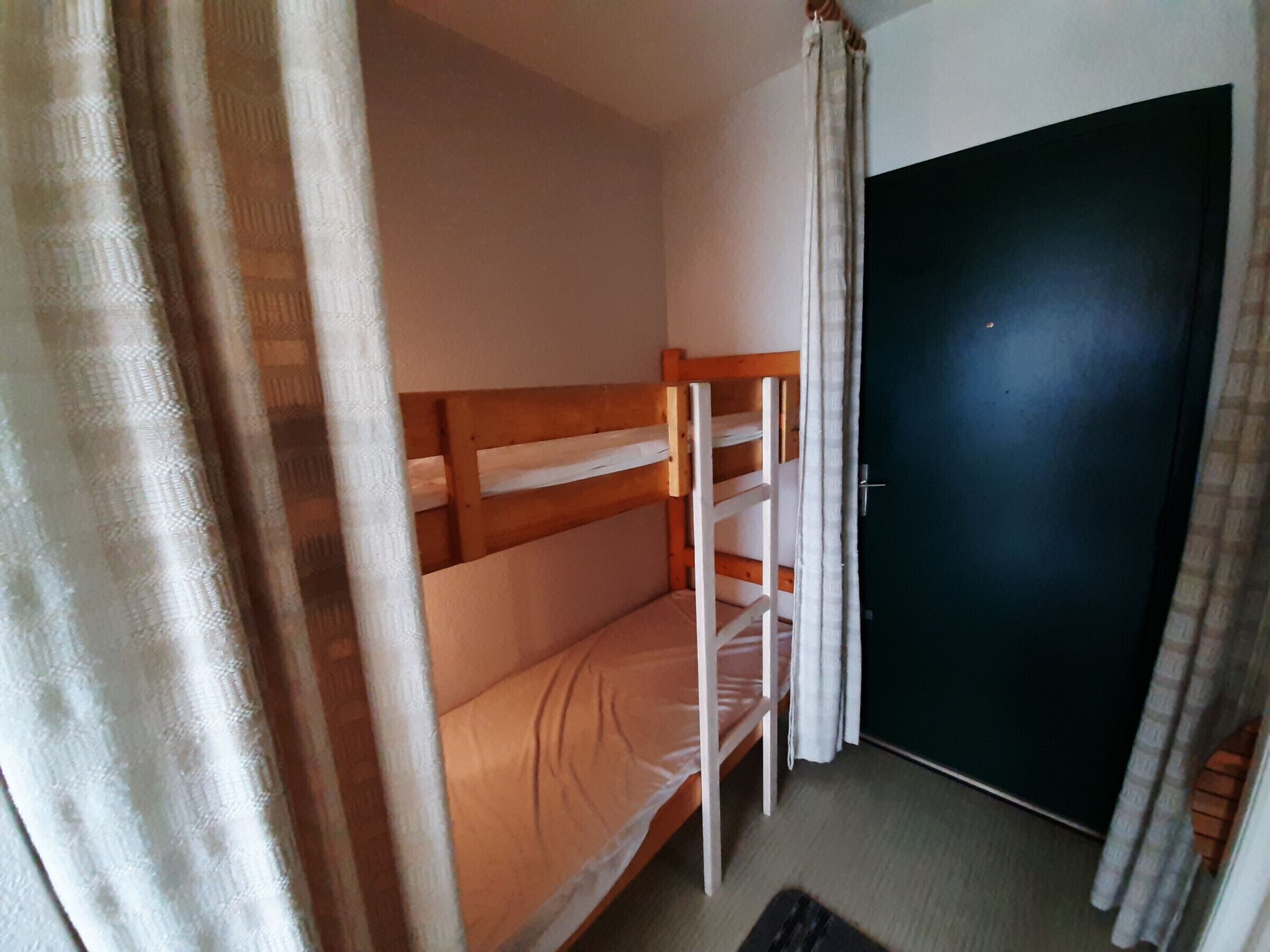 A room with a bunk bed, a door, and curtains.