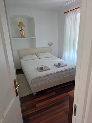 Een slaapkamer met een bed, een bedlampje, een plank en een raam met gordijnen.