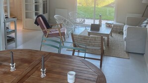 Ein modernes Wohnzimmer mit einem runden Holztisch, weißen Sofas und einer Glastür, die zu einem Garten führt.