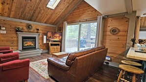Een gezellig cabin interieur met een open haard, lederen zitplaatsen, een televisie en een groot raam met uitzicht.