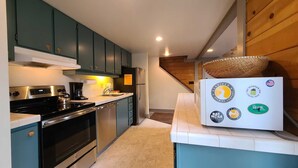 Een moderne keuken met blauwgroene kastjes, roestvrijstalen apparatuur en een witte koelkast met verschillende logo's.