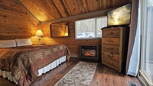 Een houten slaapkamer met een bed, een open haard, een televisie en een raam met uitzicht op auto's en bomen.