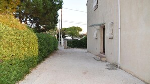 A narrow gravel path leading to a building with a concrete exterior and a small entrance. - T2 Les Lilas ,plage 300m (Hyères)
