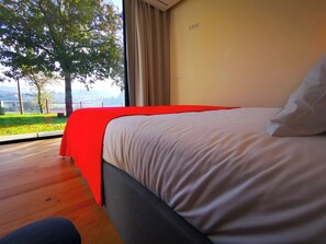 Un dormitorio con una cama grande, una ventana con cortinas y vistas a árboles y un paisaje lejano.