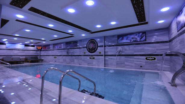 En moderne indendørs swimmingpool med flisegulv, metalstige og et loft med indbyggede spots.
