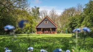 Une maison avec un toit triangulaire, une véranda avec des chaises et une pelouse parsemée de fleurs.