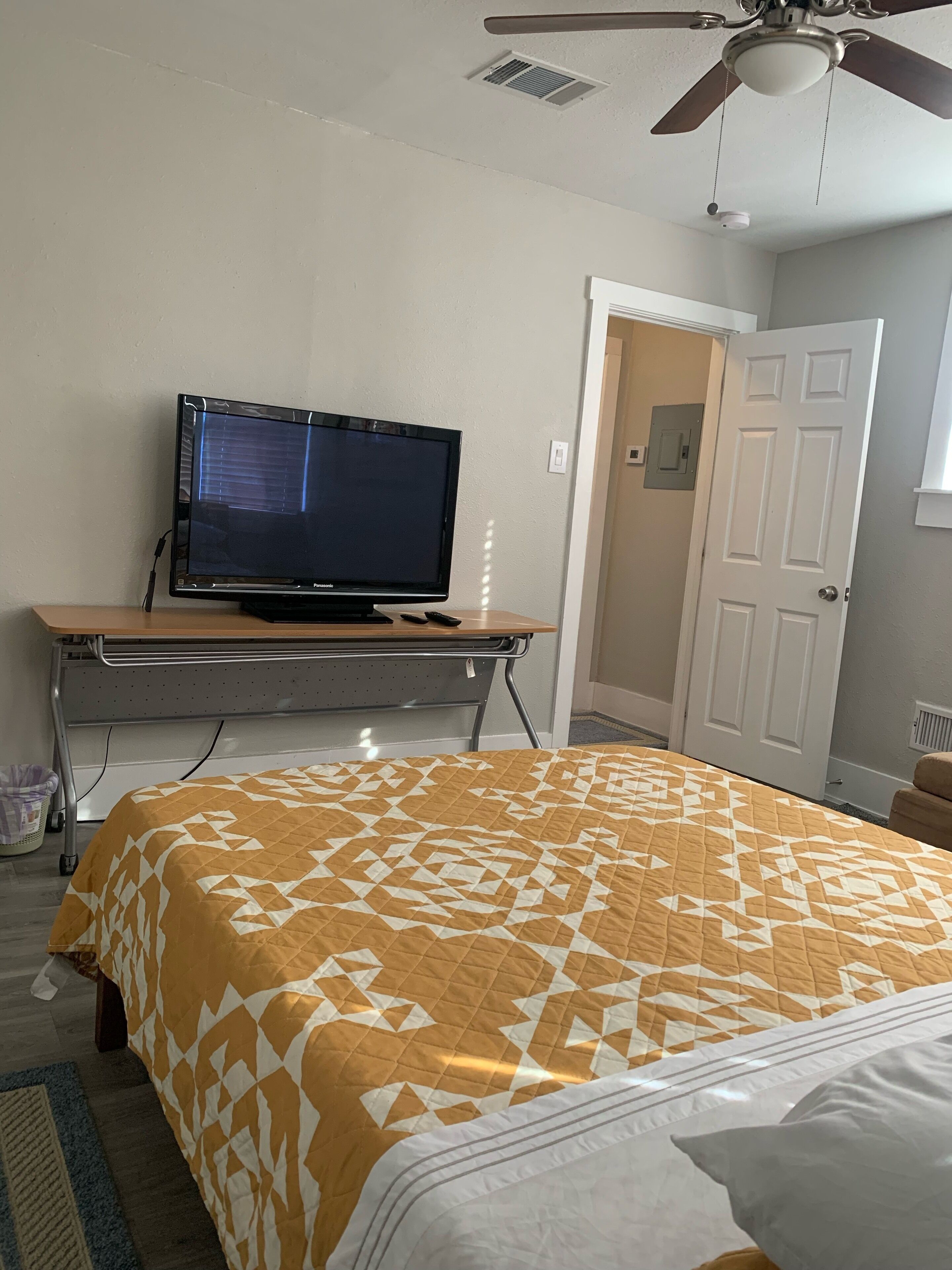 Une chambre à coucher avec un lit, un téléviseur posé sur un meuble, un ventilateur de plafond et une porte.