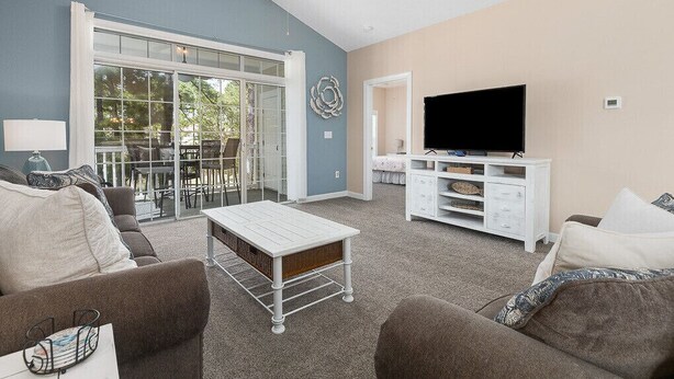A living room with a TV, white furniture, and a glass door leading to an outdoor area. - 3br/2ba condo in Barefoot Resort & Golf (North Myrtle Beach, SC)  (North Myrtle Beach)
