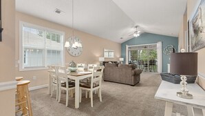 A spacious living area with a dining table, chairs, a sofa, and a large clock on the wall. - 3br/2ba condo in Barefoot Resort & Golf (North Myrtle Beach, SC)  (North Myrtle Beach)
