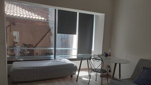 Una habitación con cama, una mesa de comedor con sillas, una ventana que da a un balcón y una pequeña cocina.