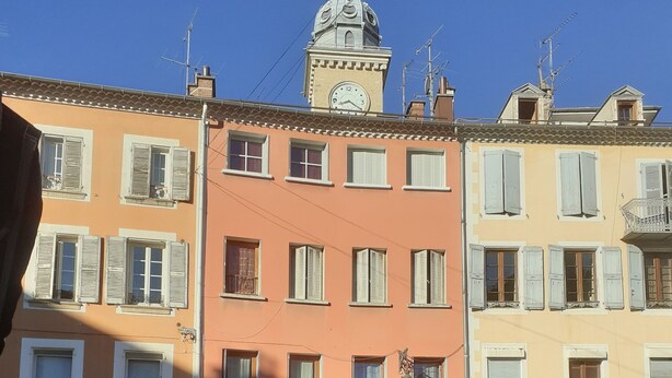 Vista de la calle con una zona de mesas de café, una tienda boutique y una torre del reloj al fondo.