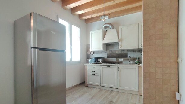 A kitchen with a stainless steel refrigerator, white cabinets, a wooden ceiling, and a tiled backsplash. - House in the woods. (Dolo)