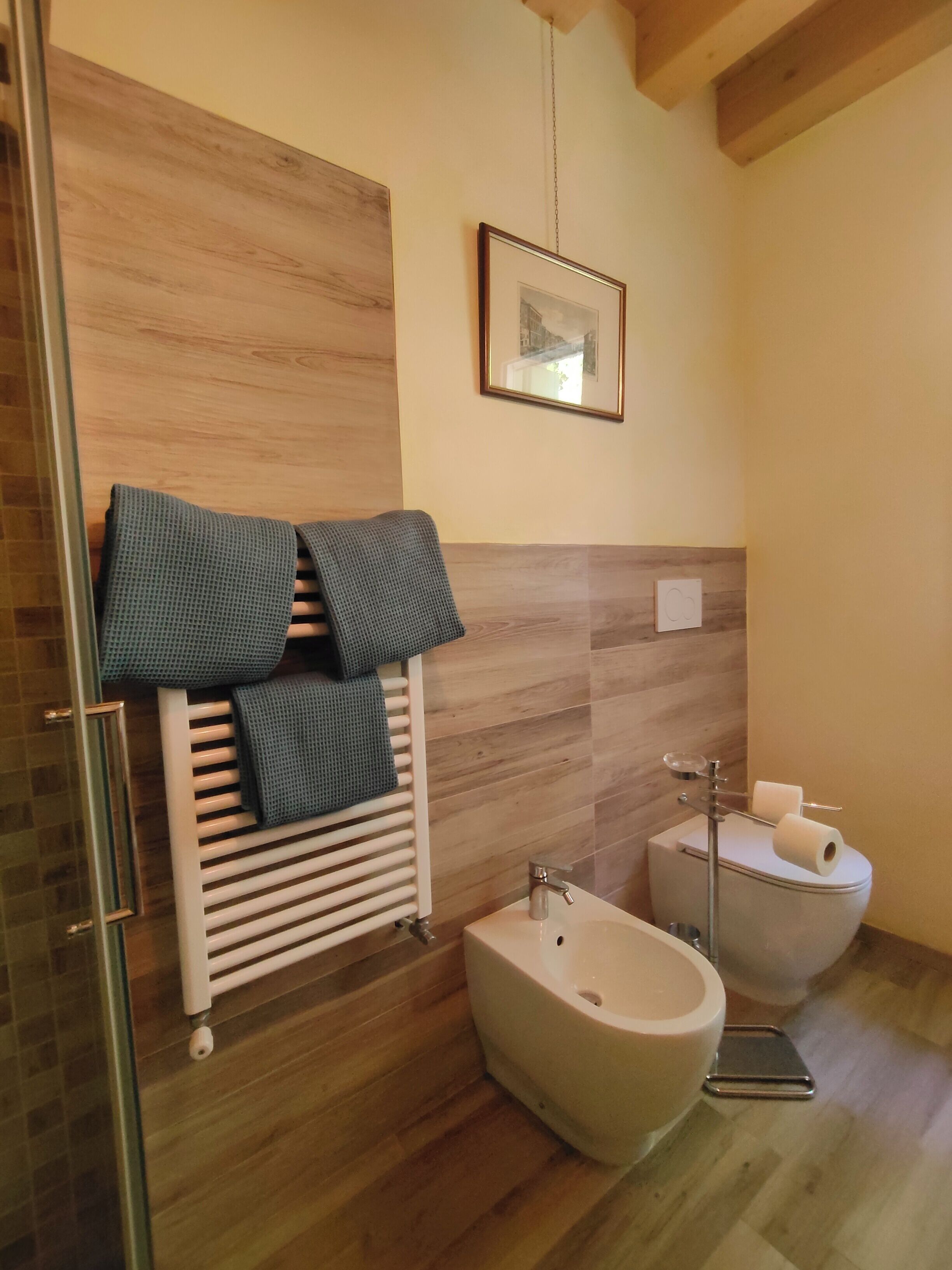 Un baño moderno con suelo de madera, un radiador blanco, un bidé y un cuadro en la pared.