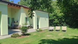 A single-story building with a covered patio area, a small garden, and outdoor seating. - House in the woods. (Dolo)