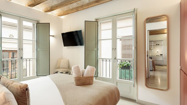 A bedroom with a bed, a TV, a large mirror, and a balcony with a view. - Modern and comfortable apartment in the heart of the city (Barcelona)