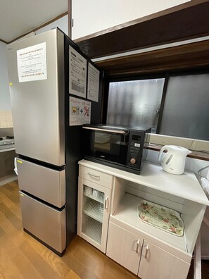 A compact kitchenette with a stainless steel refrigerator, a microwave, a kettle, and a small oven. There are cabinets with a floral-patterned mat on the countertop.