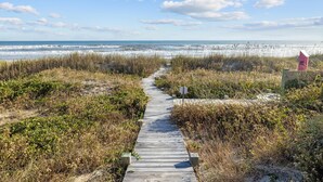 A wooden boardwalk leading to a beach with a pink lifeguard tower. - Pool - Ocean Front - Dogs OK! (Emerald Isle)