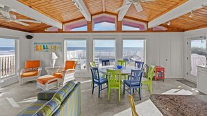 A sunroom with a wooden ceiling, large windows, a dining table with chairs, and a view of the ocean. - Pool - Ocean Front - Dogs OK! (Emerald Isle)