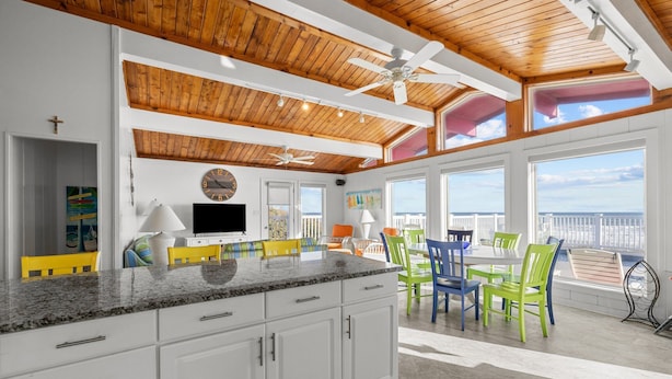 A spacious kitchen with white cabinets, granite countertops, and a dining area with colorful chairs. - Pool - Ocean Front - Dogs OK! (Emerald Isle)