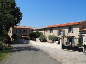 A two-story stone building with a red-tiled roof, a gravel driveway, and a black metal gate.