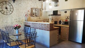 Cocina con isla de ladrillo, electrodomésticos de acero inoxidable y un comedor con sillas metálicas y un florero.