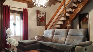 Un salón con sofá, una mesa de centro de madera, un jarrón con flores, un cuadro en la pared y una escalera.