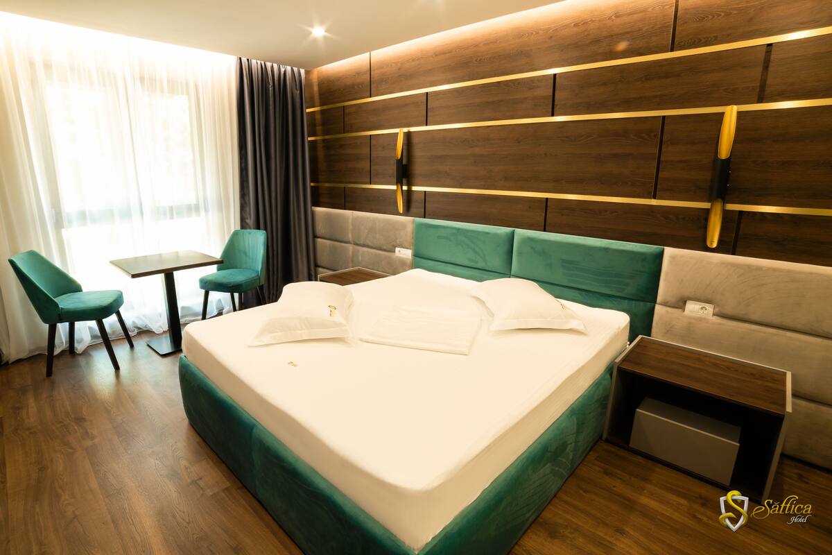 A hotel room with a large bed, a desk, a chair, and a window with curtains.